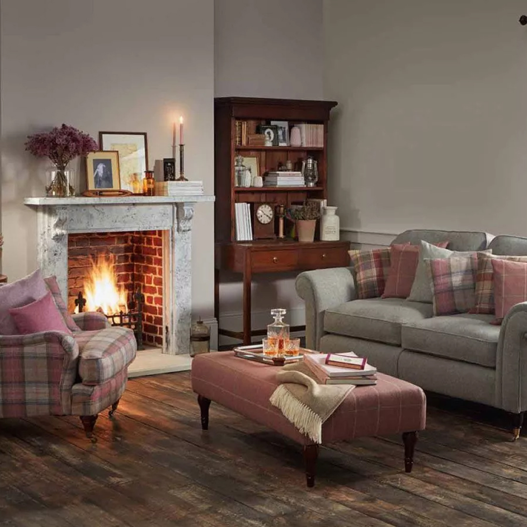 a country home with pink tweed on grey couches, a lit fire and open wood flooring